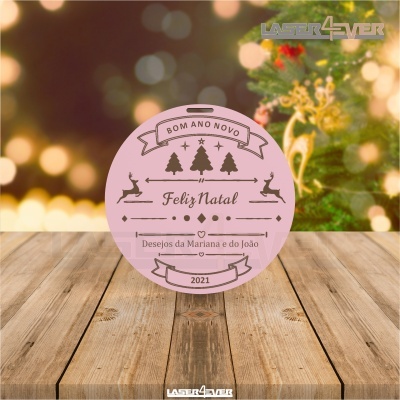 Etiqueta redonda rosa de Natal com texto e decoração natalícia sobre mesa de madeira.