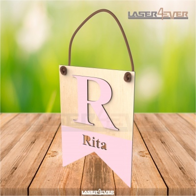 Plaquinha pendurada de madeira com letra R e nome Rita cor rosa sobre fundo verde desfocado