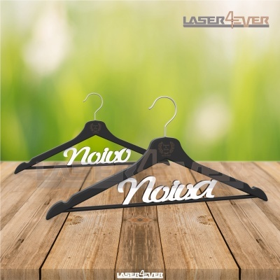 Dois cabides de madeira negra com texto 'Noiva' branco em mesa de madeira e fundo verde desfocado