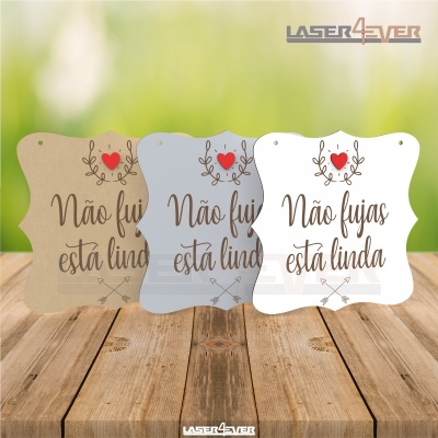 Placas decorativas com texto 'Não fujas está linda' em três cores diferentes sobre mesa de madeira