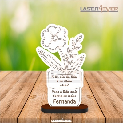 Troféu acrílico transparente com gravura de flor e mensagem para dia da mãe, sobre mesa de madeira com fundo verde