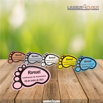 Lembranças de aniversário em forma de pegada de bebé coloridas com texto personalizado sobre mesa de madeira.