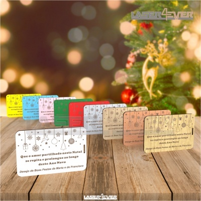 Cartões de Natal coloridos com mensagens festivas sobre mesa de madeira e árvore de Natal ao fundo