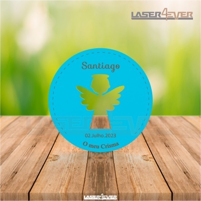 Placa redonda azul com anjo dourado e texto de crisma sobre mesa de madeira