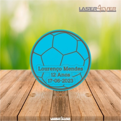 Objeto redondo azul com padrão de bola de futebol e texto personalizado sobre madeira