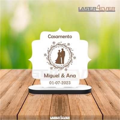 Placa de acrílico com convite de casamento branco em base preta sobre mesa de madeira