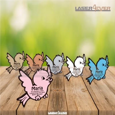 Lembranças de baby shower em formato de passarinho em acrílico colorido com texto gravado, dispostas sobre mesa de madeira