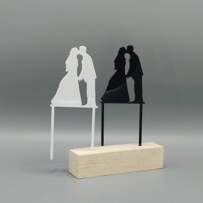 Recortes decorativos de bolo em formato de casal a beijar, um branco e outro preto, com base de madeira