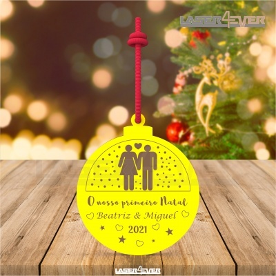 Ornamento amarelo de Natal com casal recortado, texto personalizado e cordão vermelho em madeira com fundo de árvore de Natal