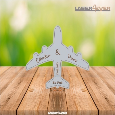 Figura decorativa em forma de avião com texto gravado, sobre tampo de madeira
