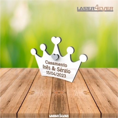 Peça decorativa branca em forma de coroa com texto de casamento, sobre mesa de madeira.