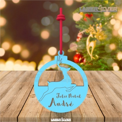 Decoração de Natal azul claro com rena e texto personalizado, pendente vermelho, sobre mesa de madeira e árvore de Natal ao fundo