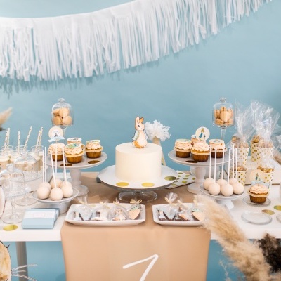 Mesa de festa decorada com bolo branco e coelho, cupcakes, cake pops e decoração azul e natural