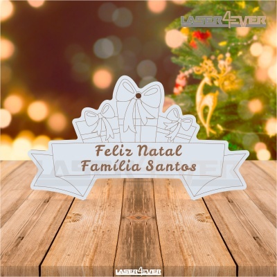 Ornamento natalício branco com texto Feliz Natal Família Santos em madeira sobre mesa de madeira com fundo festivo