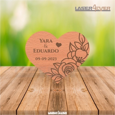 Coração em madeira gravado com nomes e data, desenho floral à direita, sobre madeira clara