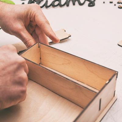 Caixa retangular de madeira clara sendo montada com fundo de madeira clara e palavra 'dreams'