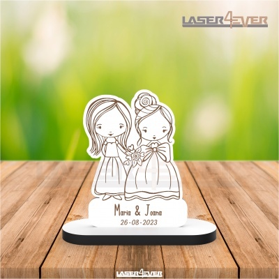 Estatueta acrílica com desenho de duas meninas e texto personalizado numa base sobre mesa de madeira