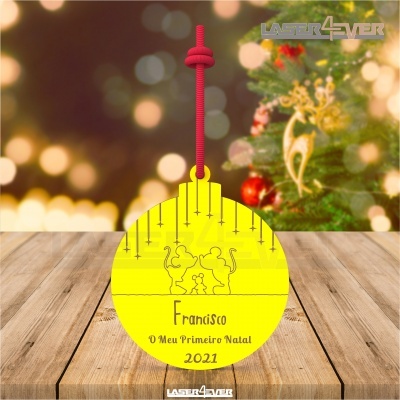 Enfeite de Natal amarelo com desenho de gatos e texto personalizado pendurado em mesa de madeira com árvore de Natal ao fundo