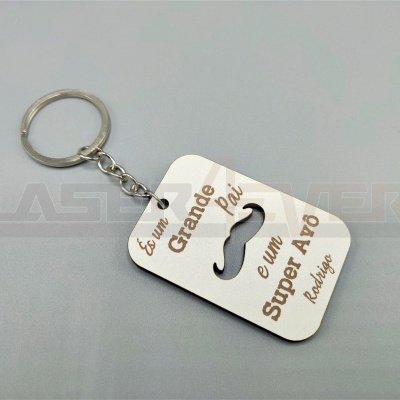 Chaveiro metálico prateado com peça branca com texto e desenho de bigode