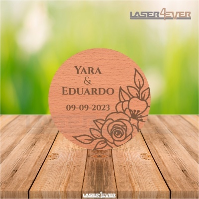 Círculo de madeira gravado com nomes e data, decorado com flores, sobre mesa de madeira