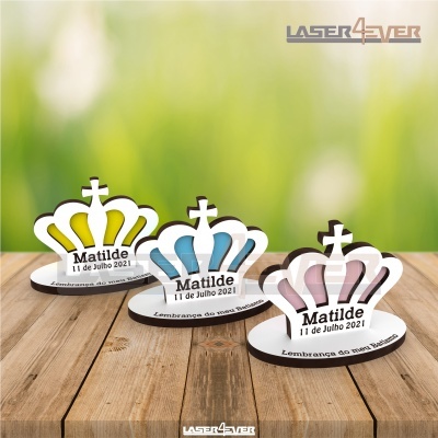 Três coroas decorativas de papel em amarelo, azul e rosa com texto para batizado