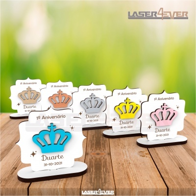 Lembranças de 1º aniversário com coroas coloridas em madeira e base branca em superfície de madeira