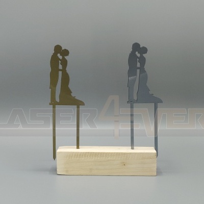Topos de bolo em metal dourado e cinzento com desenho de casal a beijar-se, sobre base de madeira clara.