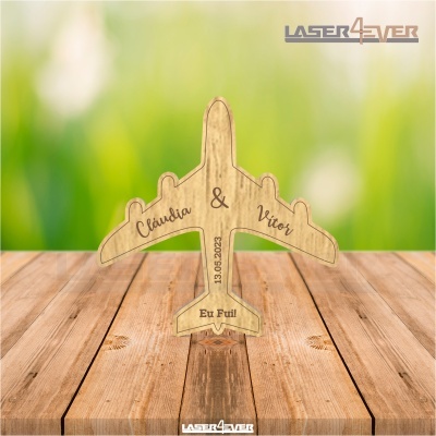 Peça decorativa de madeira em forma de avião com inscrições personalizadas sobre fundo verde desfocado