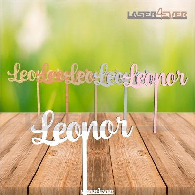 Toppers em acrílico com o nome 'Leonor' em várias cores sobre mesa de madeira