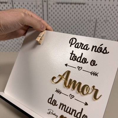Placa decorativa branca com texto em preto e dourado e detalhes de corações e setas.