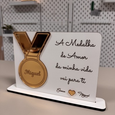 Placa decorativa branca com medalha dourada espelhada e texto em português
