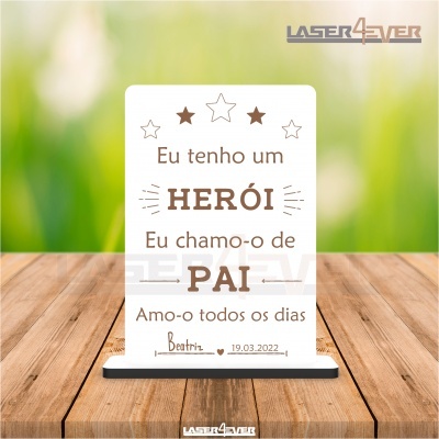 Placa decorativa branca com texto sentimental em português e estrelas, sobre mesa de madeira, fundo desfocado verde