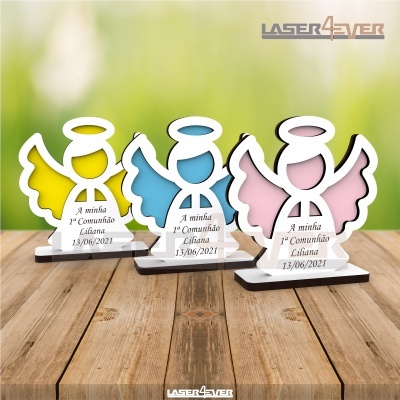 Três lembranças de comunhão em formato de anjo nas cores amarelo, azul e rosa sobre madeira.