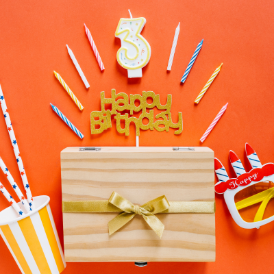 Caixa de madeira com fita dourada e artigos de festa como velas e óculos coloridos