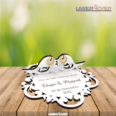 Decoração de madeira branca com corações entrelaçados e pássaros, texto gravado com nomes e data, sobre mesa de madeira