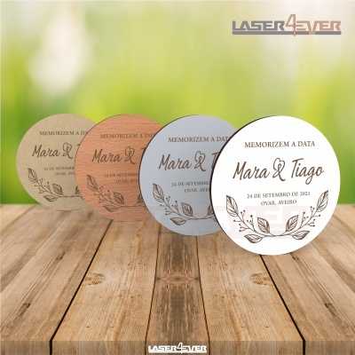 Convites redondos para casamento com nomes Mara & Tiago e data 24 de setembro de 2021, em várias cores, sobre mesa de madeira.