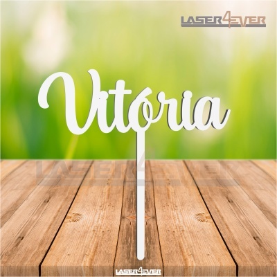 Topo de bolo branco com a palavra 'Vitória' em letra cursiva num pau branco sobre madeira rústica