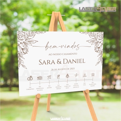 Placa de boas-vindas de casamento com texto e desenhos florais em tripé de madeira numa área exterior verde