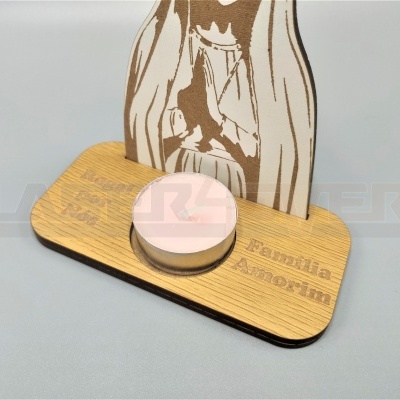 Porta-vela decorativo em madeira com vela rosa e figura recortada de uma pessoa a orar.