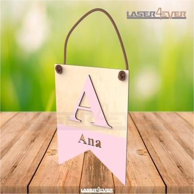 Placa decorativa de madeira com letra A grande e nome Ana pintados em rosa e preto, pendurada por corda em fundo verde.