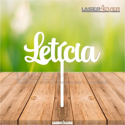 Letreiro branco em MDF com o nome 'Letícia' em letra cursiva sobre mesa de madeira clara.