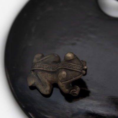 Estatueta pequena em metal com formato de sapo decorado sobre superfície preta