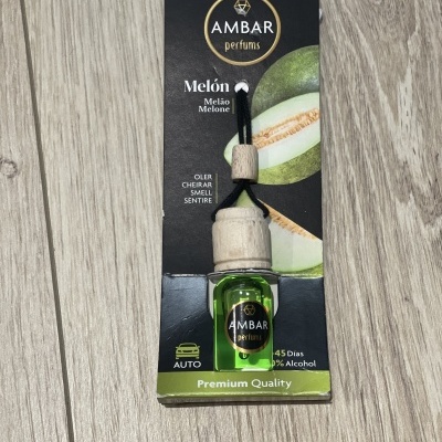 Parfum auto AMBAR Melón avec bouteille verte et bouchon en bois sur boîte noire et verte avec images de melon