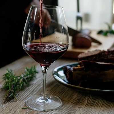 Copo de vinho tinto sendo enchido com carne e alecrim ao fundo