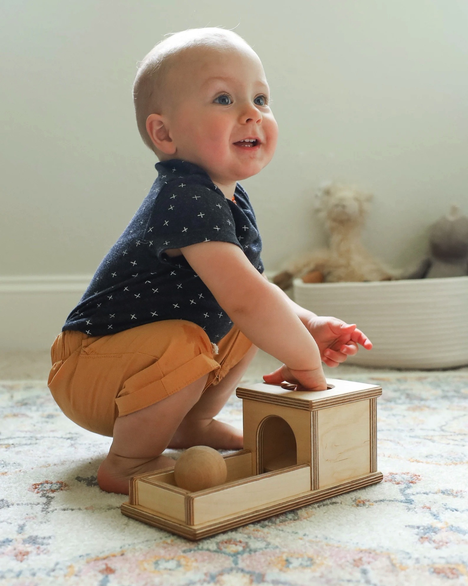 Criança a brincar com brinquedo de madeira numa sala com tapete e cesto branco ao fundo