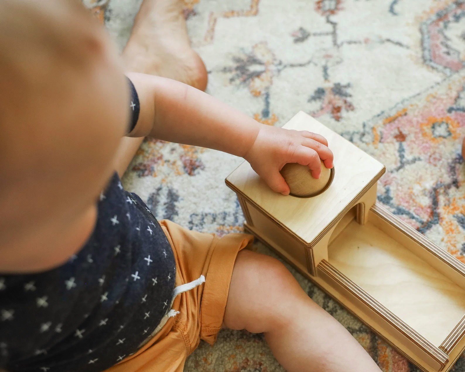Criança a usar brinquedo de madeira com bola, sobre tapete colorido