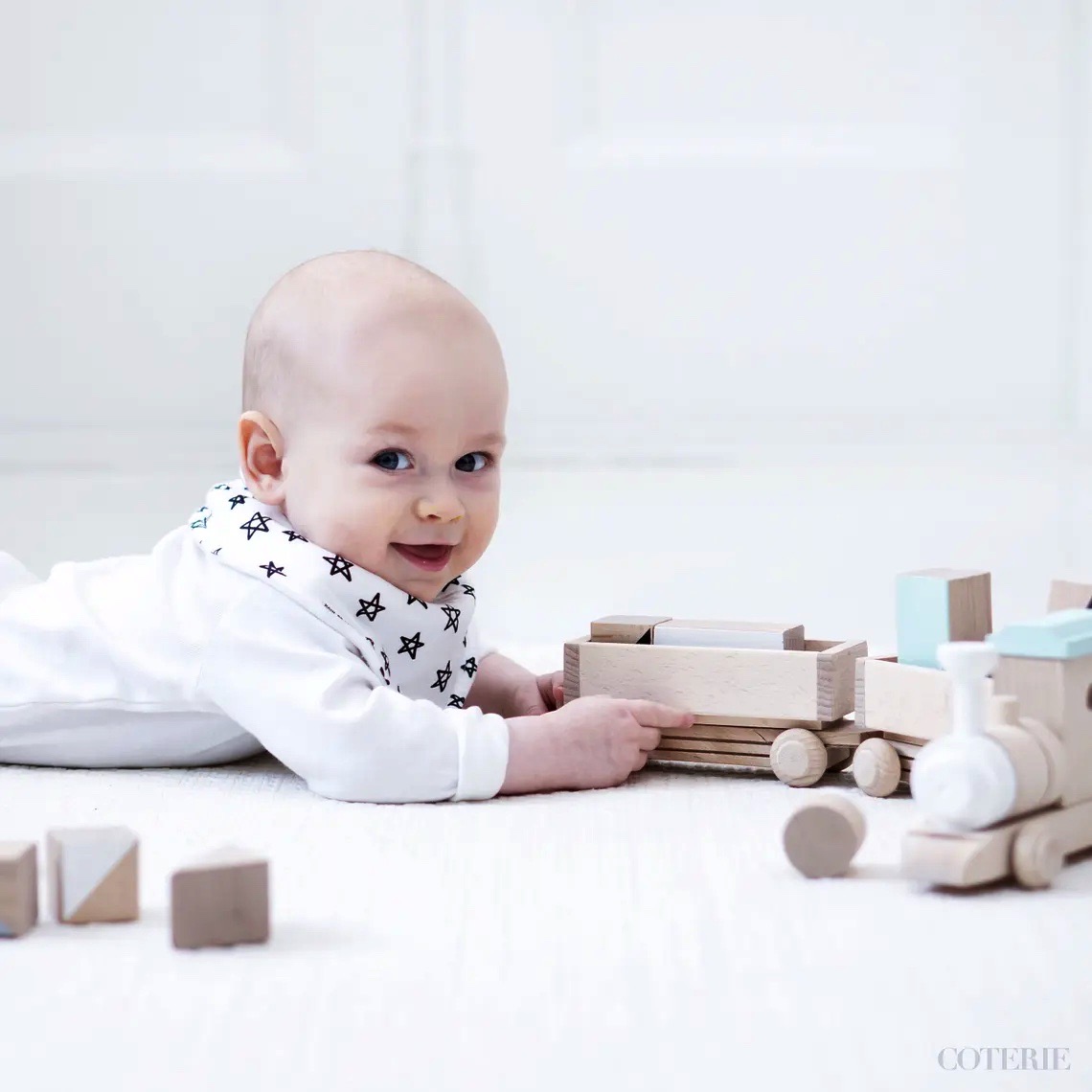 Bebé deitado a brincar com comboio de brinquedo de madeira em chão claro