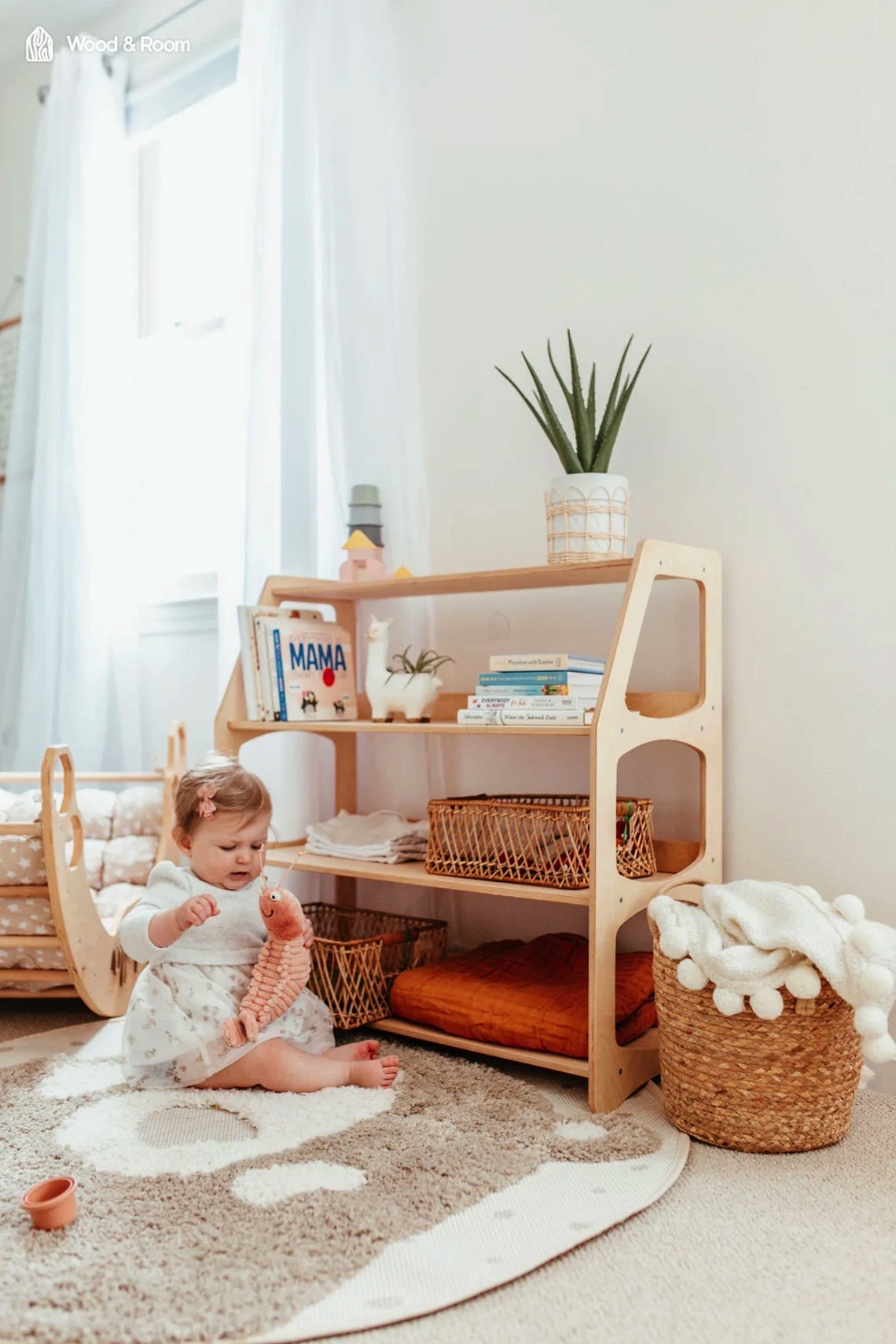 Estante infantil de madeira com livros, plantas, cestos e mantas num quarto claro com carpete e janela
