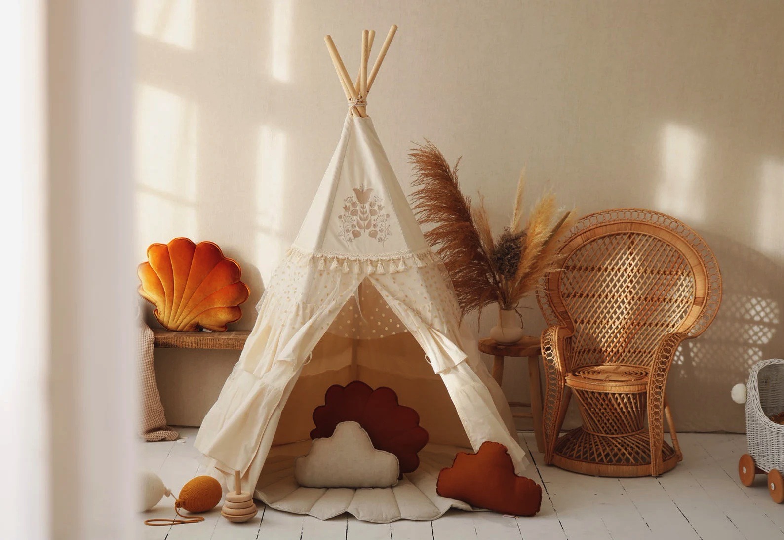 Tenda de brinquedo tipo tipi branca com almofadas e cadeira de vime num ambiente claro