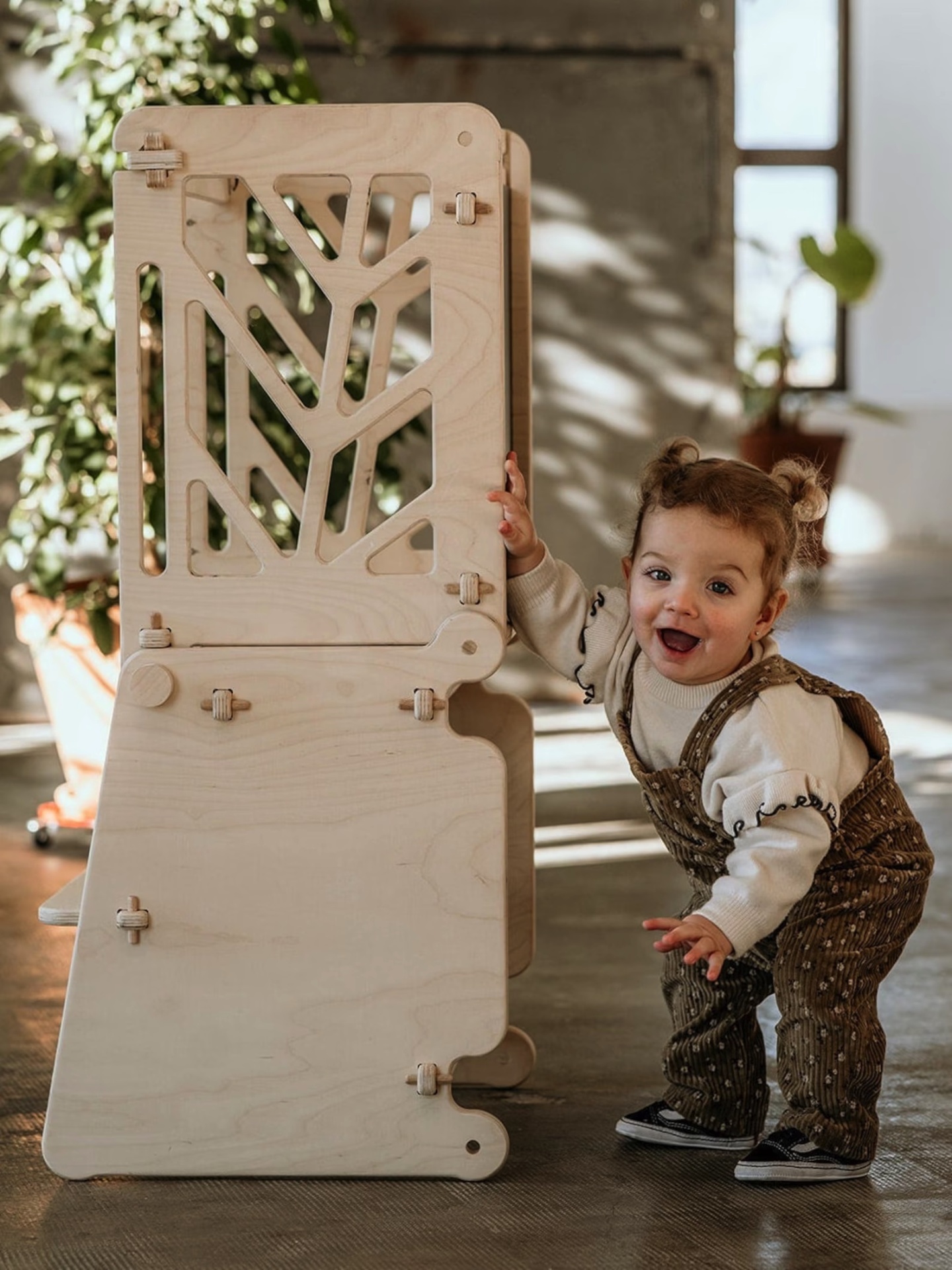 Estrutura de madeira clara com desenho recortado e criança pequena a interactuar com ela em ambiente interior
